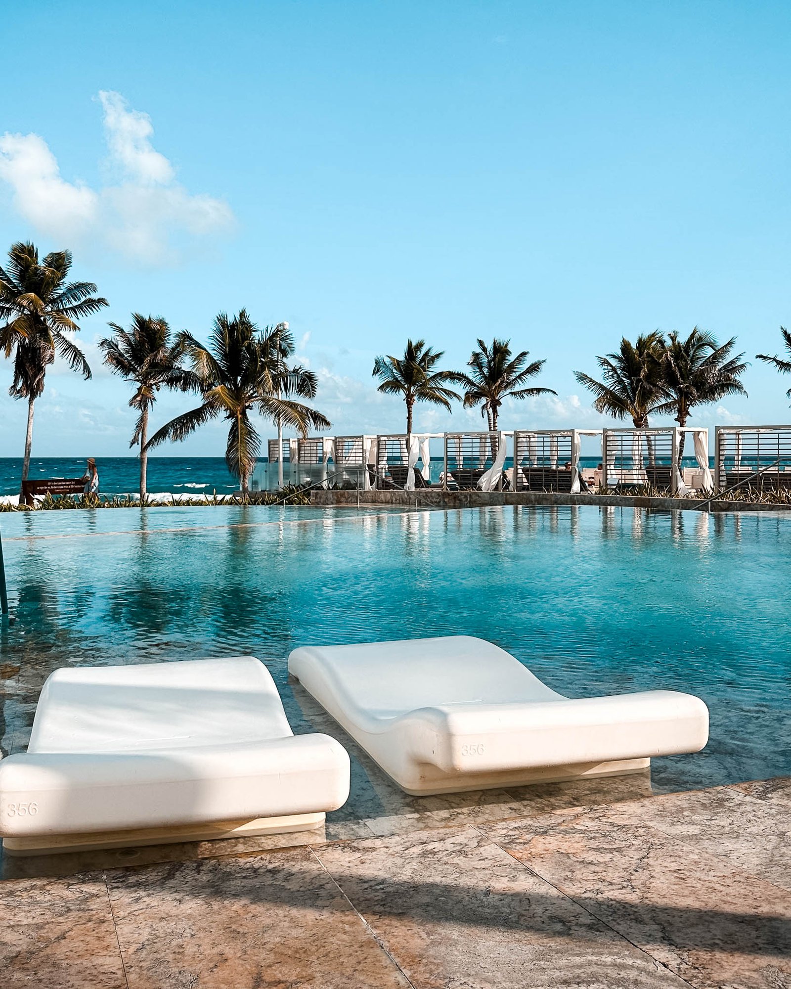Poolbereich des TRS Yucatan Hotel mit Wasserliegen am Pool, dahinter Palmen und Bali Betten