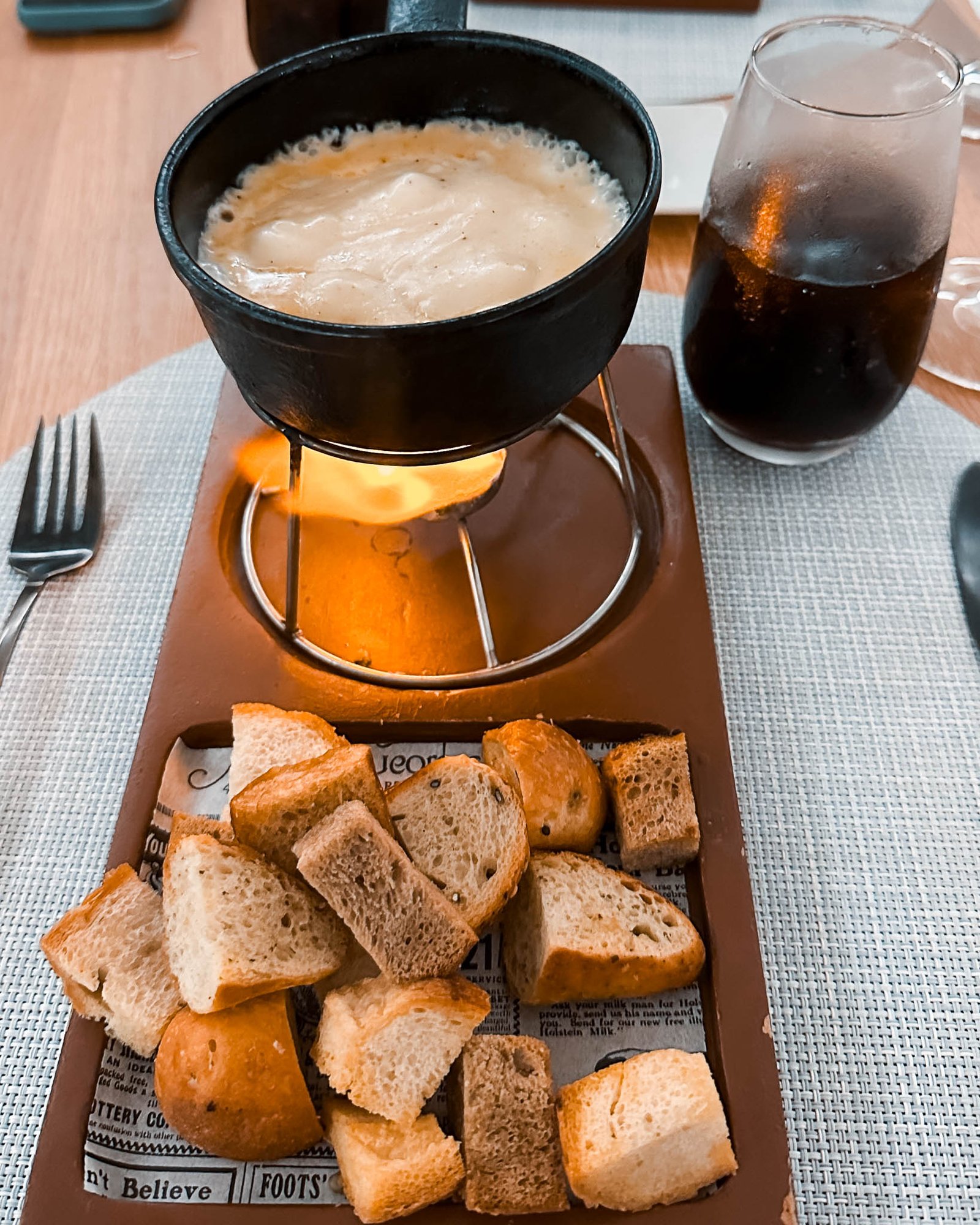 Käsefondue in einem Stahltopf mit Brot und Coca Cola