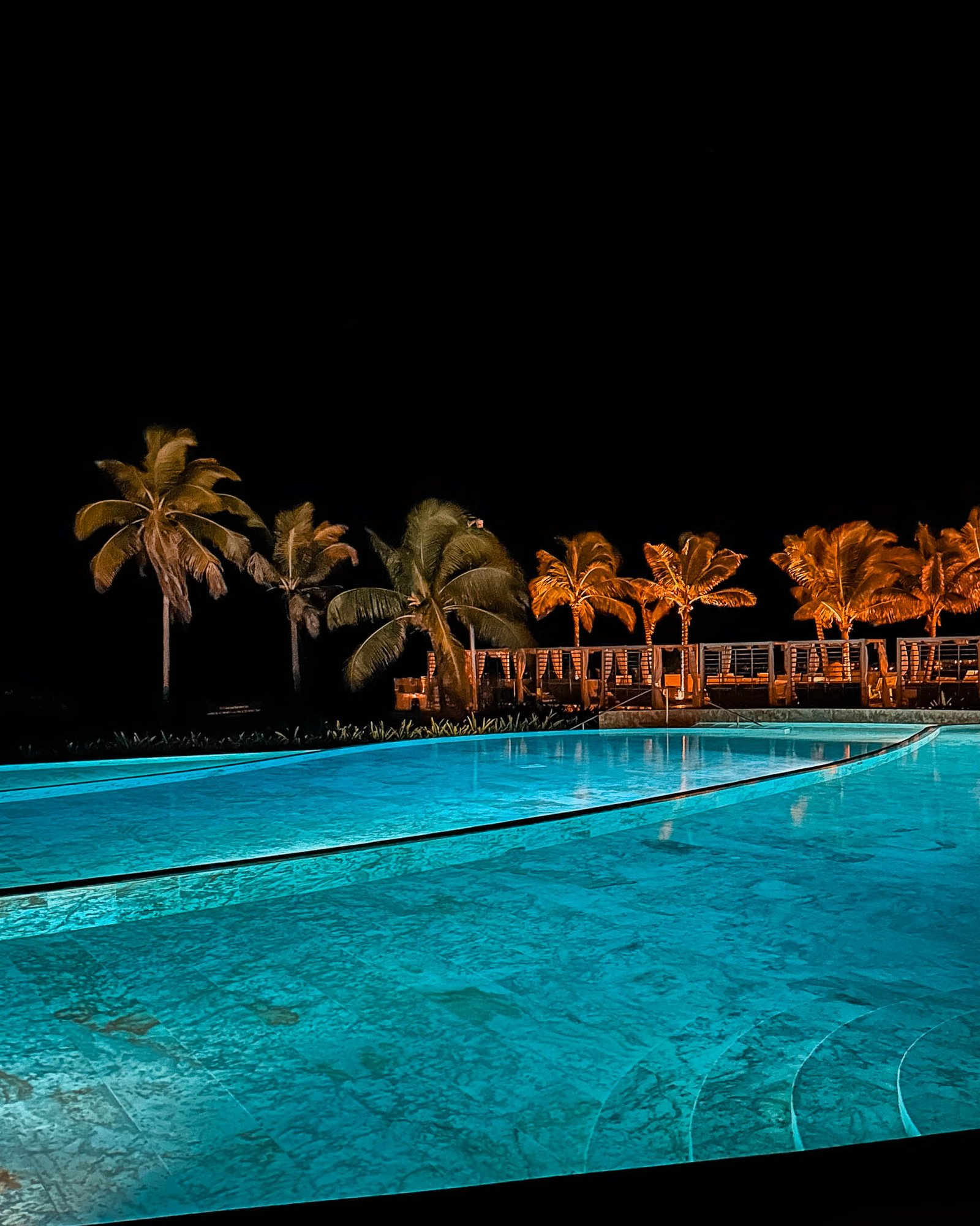 Der beleuchtete Pool und die beleuchteten Palmen dahinter im Hotel am Abend