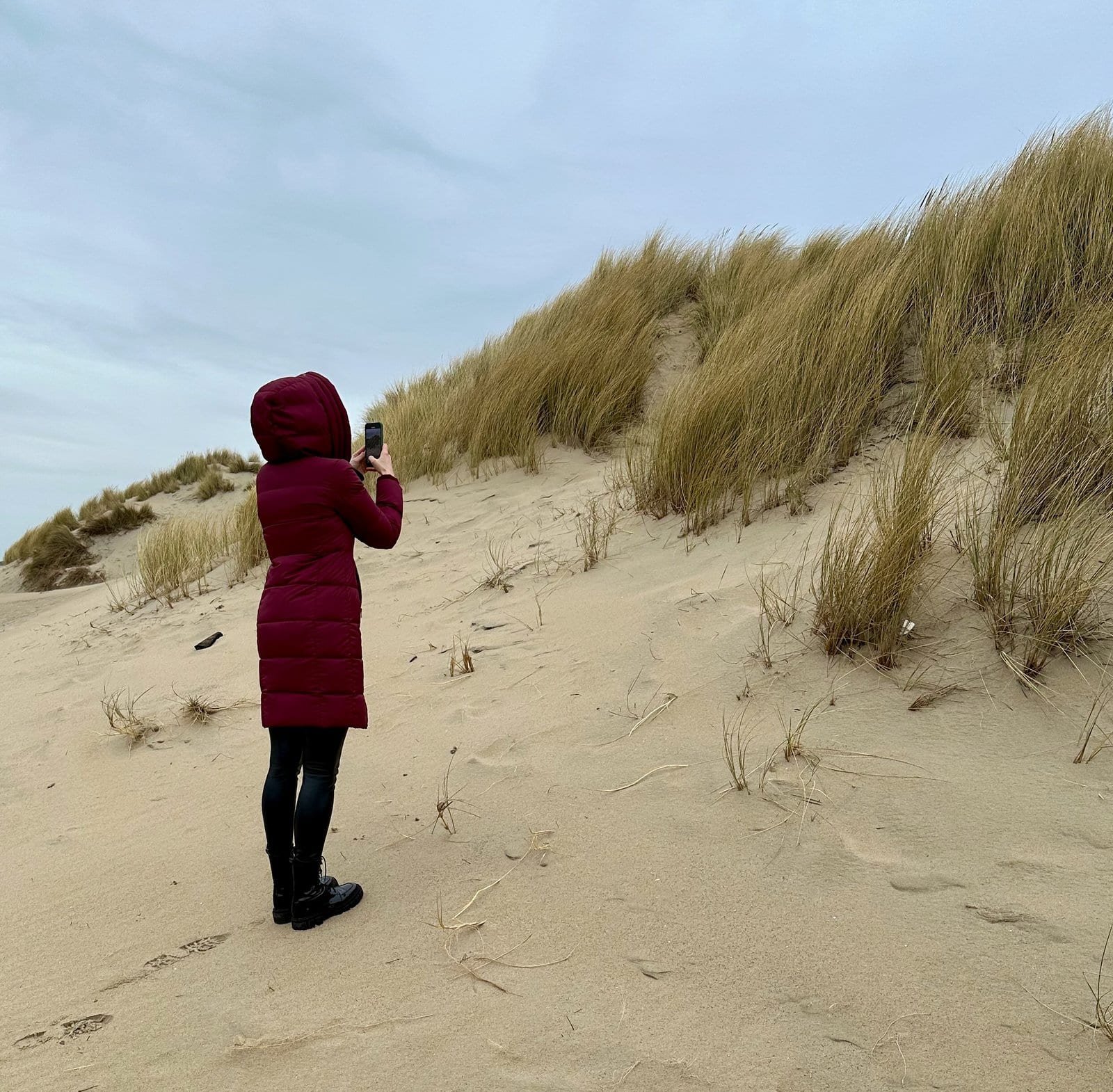 Frau in roter Jacke fotografiert Dünen am Strand