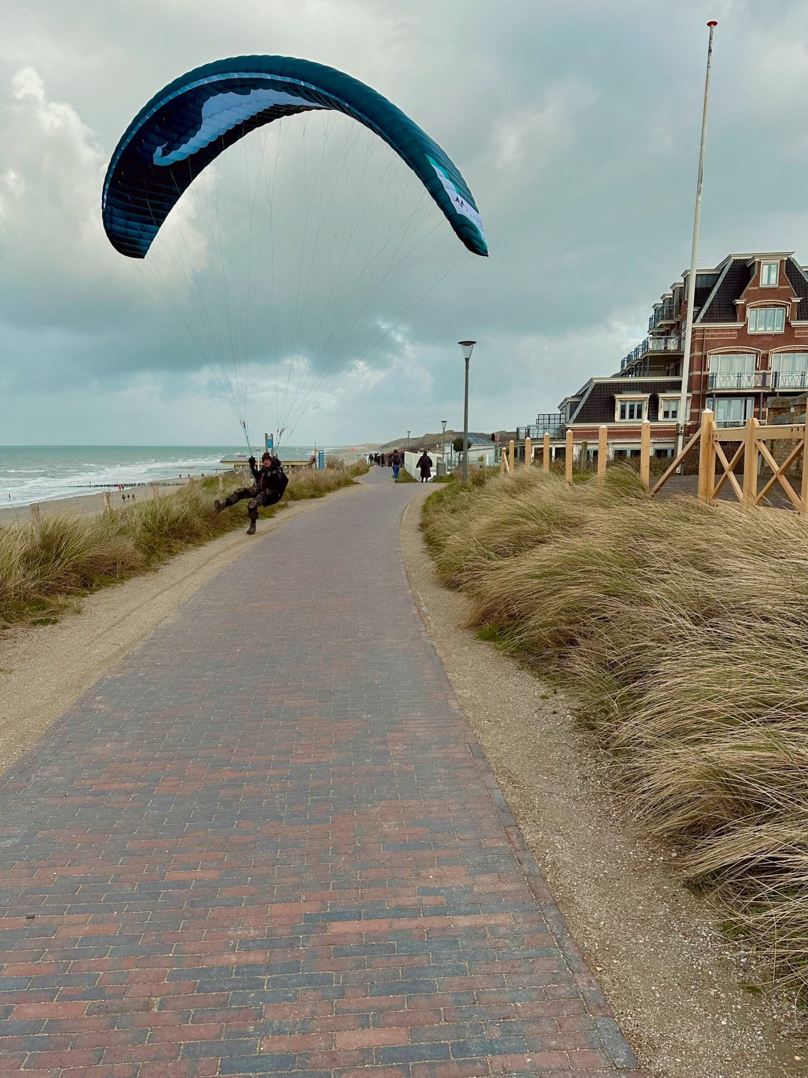 Weg auf dem Damm mit Blick auf Luxushotel davor ein Paraglider