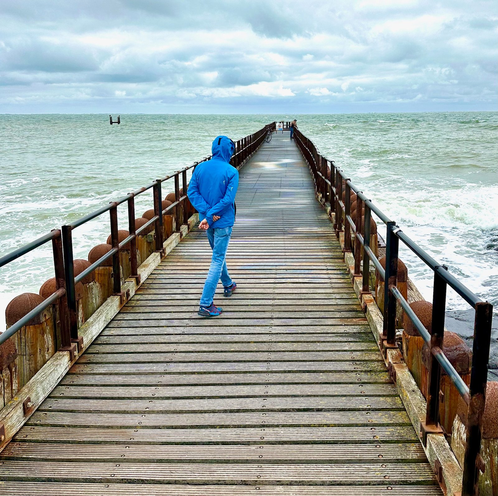 Mann läuft über Steg der ins Meer ragt und von Wellen geflutet wird